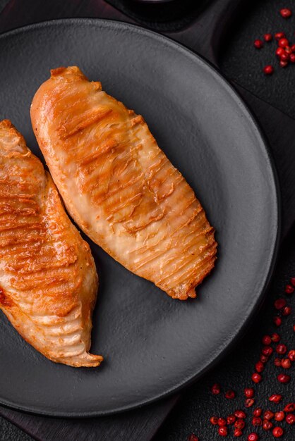 Delicious fresh grilled chicken fillet with spices and herbs on a dark concrete background