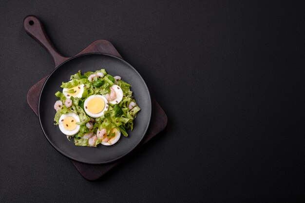 Delicious fresh healthy salad with shrimp egg lettuce and flax seeds on a black ceramic plate on a concrete background