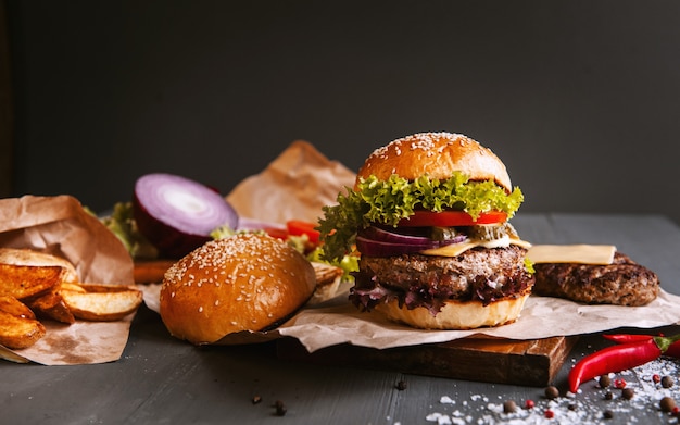 Delicious fresh homemade burger on a wooden table. next to the component to burger, wooden trays, fried potatoes and chili pepper.