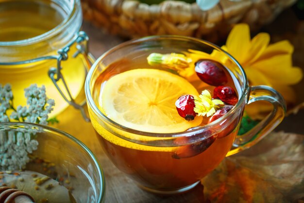 Miele fresco delizioso e una tazza di tè sano con il limone e i cinorrodi su una tavola di legno