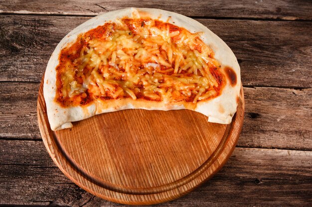 Delicious fresh italian folded stuffed pizza calzone with baked cheese served on wooden platter on dark rustic table, top view.