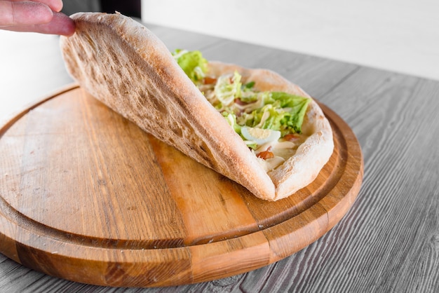 Delicious fresh italian pizza with ham, salami, tomatoes, salad, quail egg and parmesan on a wooden board on a wooden table. Perfect pizza dough.