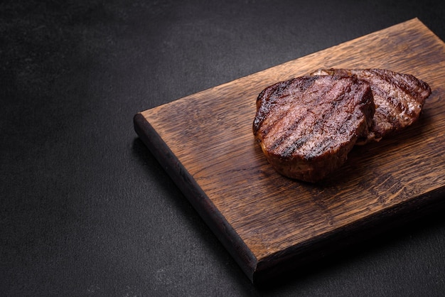 Delicious fresh juicy beef steak with spices and herbs on a dark concrete background