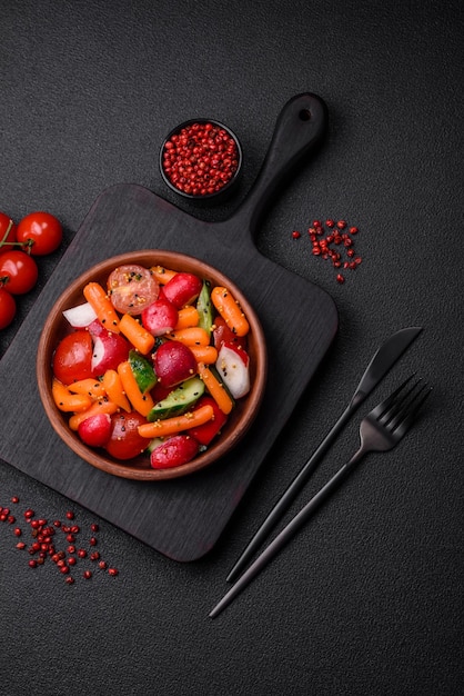 Вкусный свежий сочный салат с редицами помидорами морковими огурцами специями и травами на темном бетонном фоне