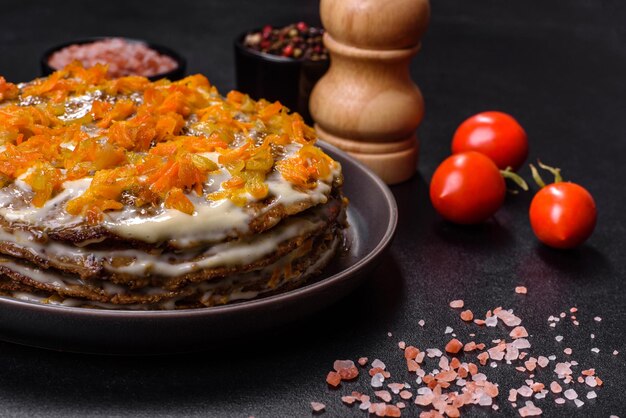 Delicious fresh liver cake with mayonnaise and carrots on a black plate against a dark concrete background