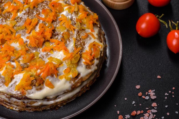 Delicious fresh liver cake with mayonnaise and carrots on a black plate against a dark concrete background