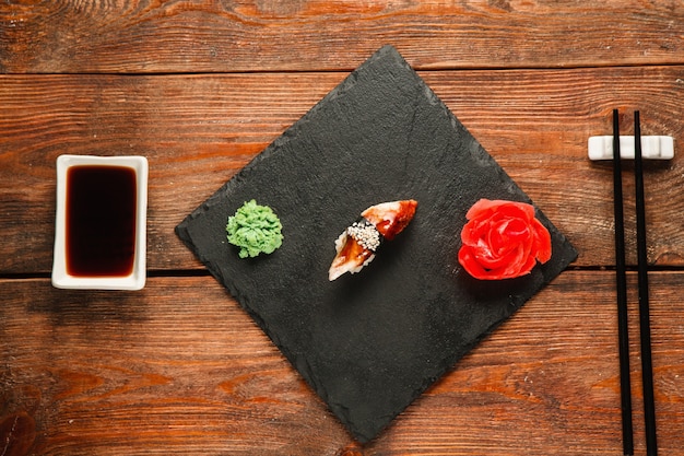 Delicious fresh nigiri with smoked eel served on black slate with ginger and wasabi, on wooden rustic table, flat lay. Japanese healthy seafood, traditional cuisine.