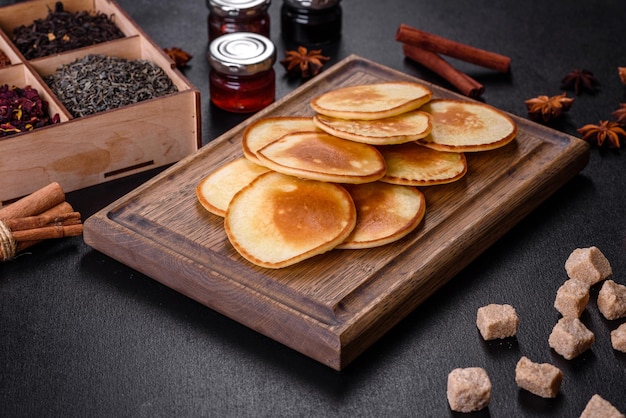 Delicious fresh pancakes on a wooden cutting board with sugar on a dark concrete background