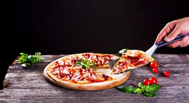 木製の背景にベーコンとトマトペーストのおいしい新鮮なピザ。上面図。