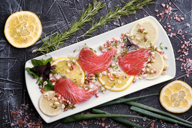 Photo delicious fresh raw tuna on a white plate with lemon pieces, greens and rosemary on the background, top view, close-up.