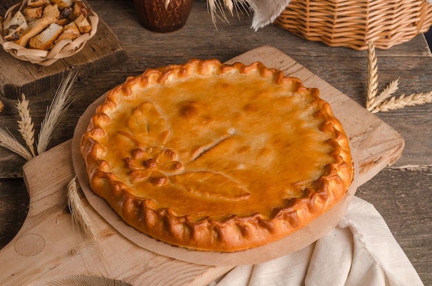 Delicious fresh round pie stuffed with curly dough decorations on wooden background