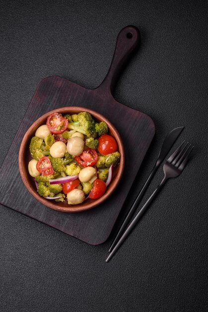 Delicious fresh salad with broccoli cherry tomatoes mushrooms onions salt spices and herbs on a dark concrete background