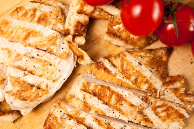 Delicious Fresh sliced grilled chicken breast on wooden board next to a bunch of tomatoes. Healthy dinner and lifestyle