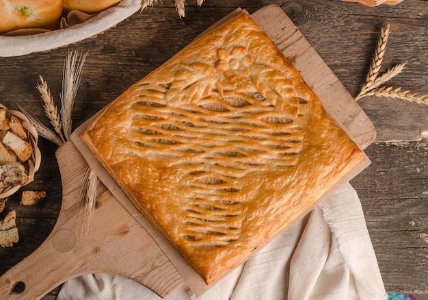 Delicious fresh square pie stuffed with curly dough decorations on wooden background