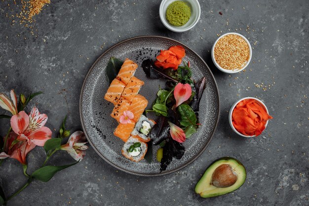 Deliziosi rotoli di sushi freschi con salmone e formaggio filadelfia su lastra grigia su sfondo di pietra scura