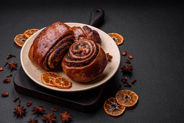 Delicious fresh sweet baked buns with poppy seeds and cinnamon on a ceramic plate on a dark concrete background