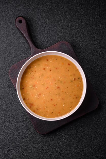 Delicious fresh vegetable soup with carrots peppers potatoes and onions in a white ceramic plate on a dark concrete background