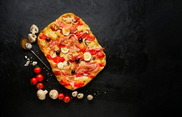 Delicious freshly baked square pizza with ham, cheese and olives on black background with ingredients, top view