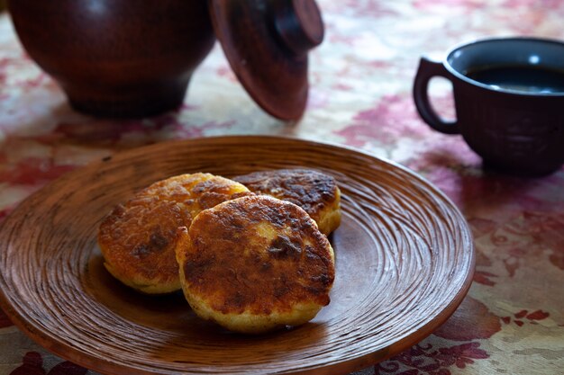 Вкусные жареные сырники на глиняной тарелке в деревенской обстановке.