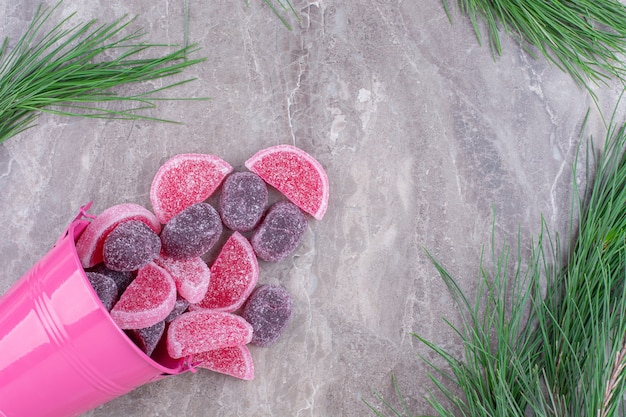 Delicious fruit jelly candies out of pink bucket on stone.