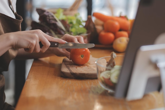 Delicious fruit and vegetables on a table and woman cooking Housewife is cutting green cucumbers on a wooden board for making fresh salad in the kitchen