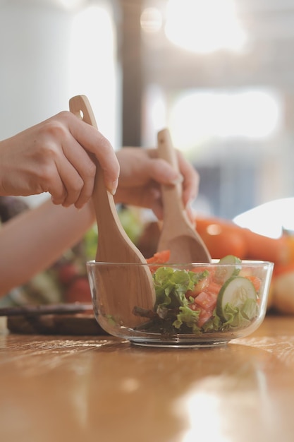 テーブルに美味しい果物と野菜があり女性が料理をしています主婦はキッチンで新鮮なサラダを作るために木製の板に緑のキュウリを切っています