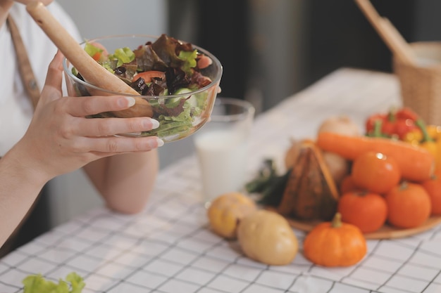 맛있는 과일과 채소가 테이블 위에 있고 여자가 요리하고 있습니다. 집주인이 부에서 신선한 러드를 만들기 위해 나무판에 녹색 호박을 잘라내고 있습니다.