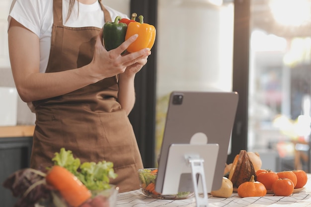 На столе вкусные фрукты и овощи, а женщина готовит. Домохозяйка режет зеленые огурцы на деревянной доске для приготовления свежего салата на кухне.