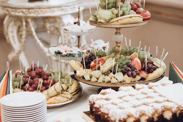 Photo delicious fruits on stand and desserts sweet on table at wedding reception in restaurant luxury catering christmas feast wedding candy bar