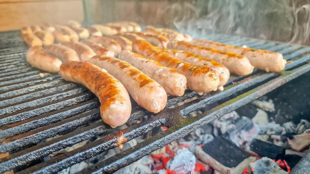 바비큐 그릴에서 고기를 요리하는 바비큐 그릴맨의 석탄 위에서 지글거리는 맛있는 독일 소시지