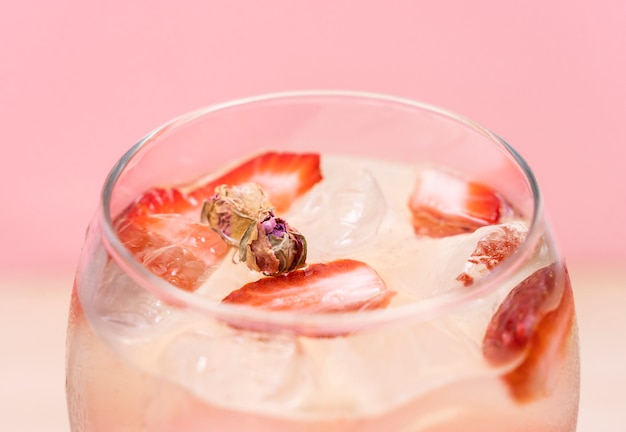 Delicious Gin Tonic cocktail decorated with cinnamon roll strawberry and mint on a pink background