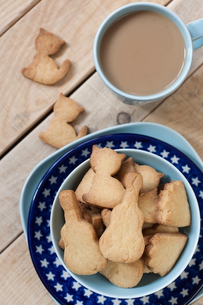 Вкусные пряники, приготовленные на синюю тарелку, чашка кофе из молока на легкий деревянный стол.