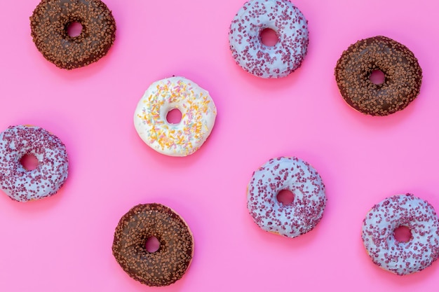 Вкусные глазированные пончики на розовой поверхности Плоский минималистский пищевой арт-фон Вид сверху