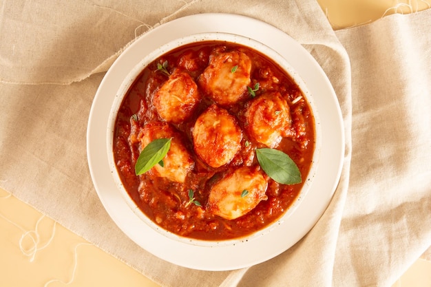 Delicious Gnocchi with Red Sauce and Basil served in a White textured Handmade Ceramic Bowl in a beige fabric background in top view