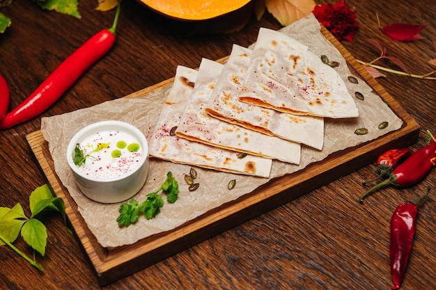 Delicious gourmet flat bread kutabs with herbs and cheese on a wooden board with sauce