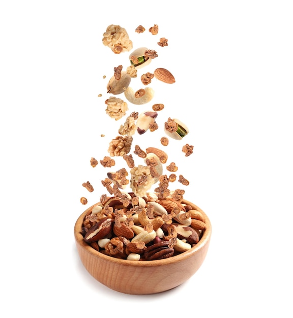 Delicious granola and nuts falling into bowl on white background Healthy snack