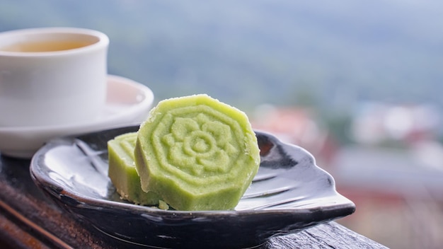 Delicious green mung bean cake with black tea plate on wooden railing of a teahouse in Taiwan with beautiful landscape in background close up