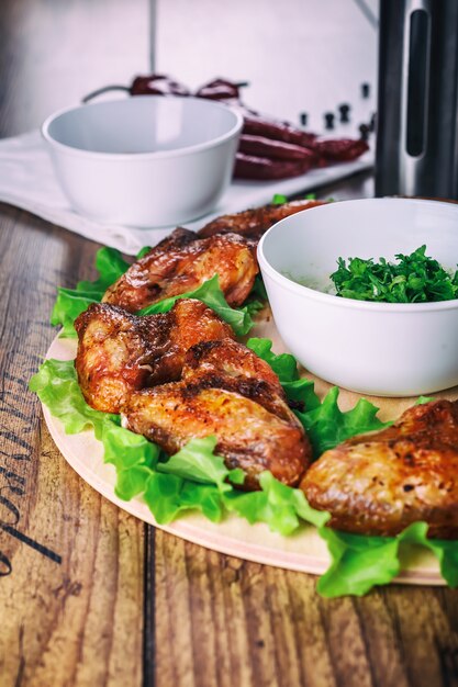 Delicious grilled chicken wings with garlic and tomato sauce with lettuce on a round board on wooden rustic background