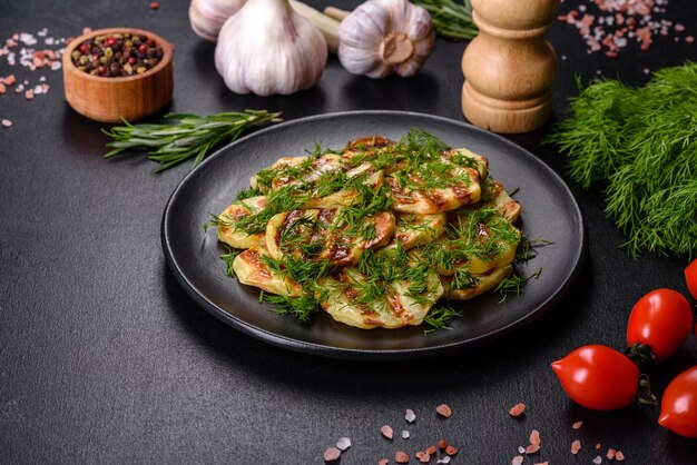 Delicious grilled potato slices with spices and herbs on a black plate