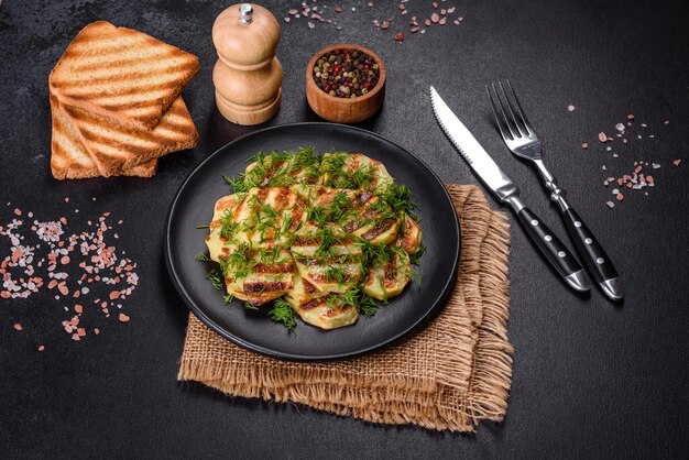 Delicious grilled potato slices with spices and herbs on a black plate