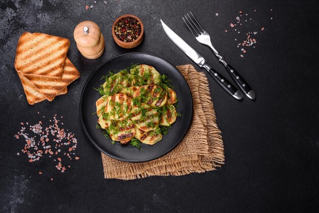 Delicious grilled potato slices with spices and herbs on a black plate