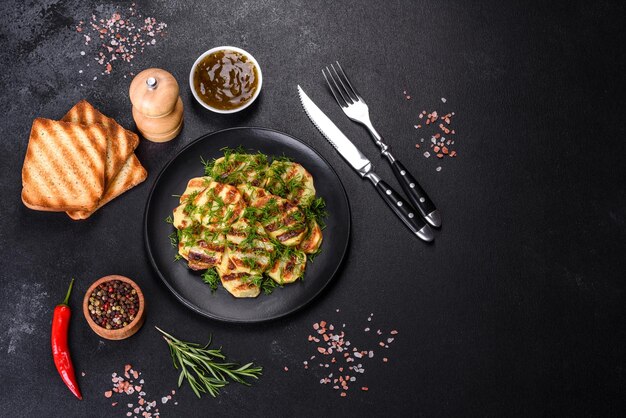 Delicious grilled potato slices with spices and herbs on a black plate