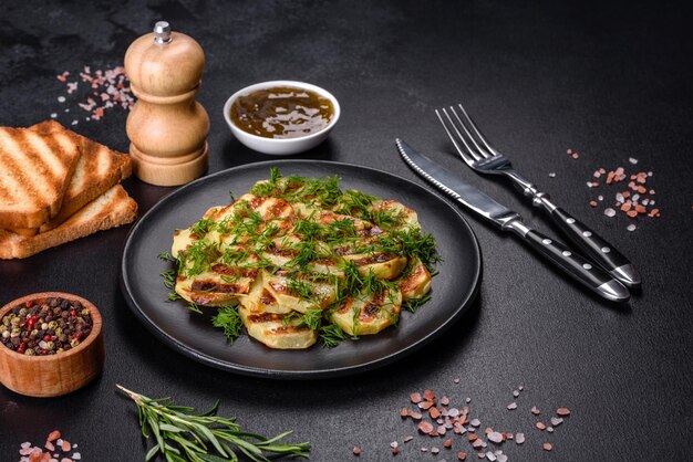 Delicious grilled potato slices with spices and herbs on a black plate