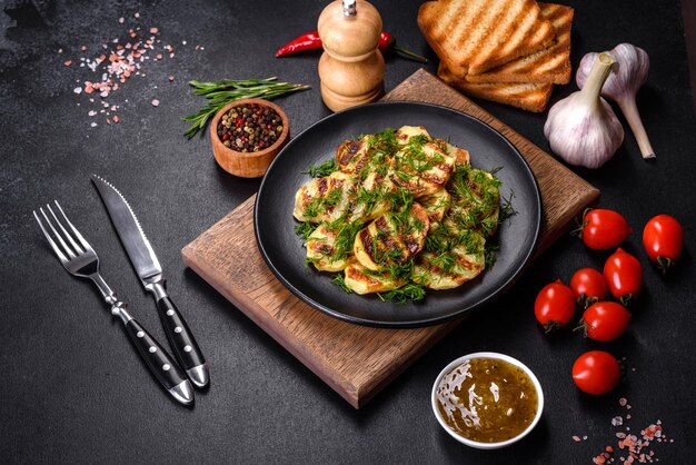 Delicious grilled potato slices with spices and herbs on a black plate