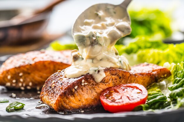 Delicious grilled roasted salmon fillets or steaks with mushroom sauce sesame tomatoes and lettuce salad.