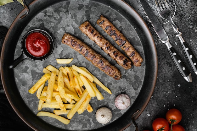 Delicious grilled sausages and vegetables on black dark stone table background top view flat lay