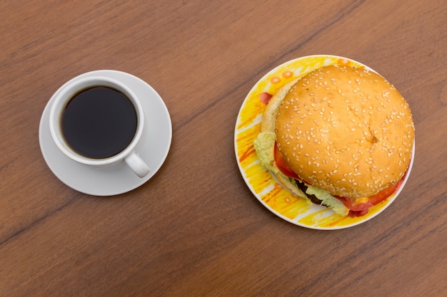 Delicious hamburger and cup of coffee on wooden table. Top view