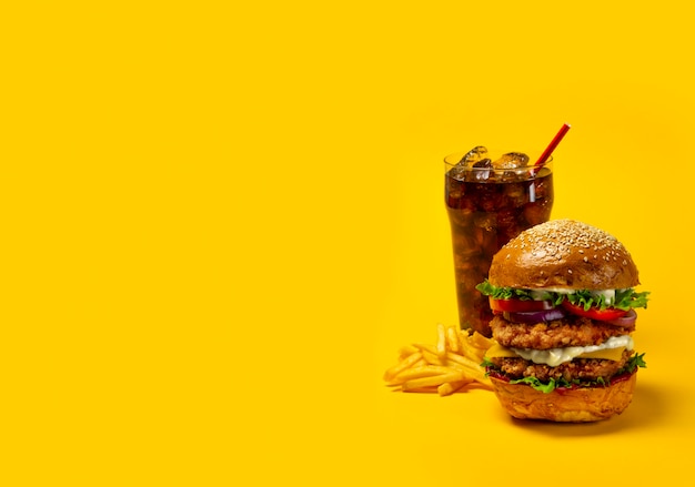 Delicious hamburger with cola and potato fries on a yellow background