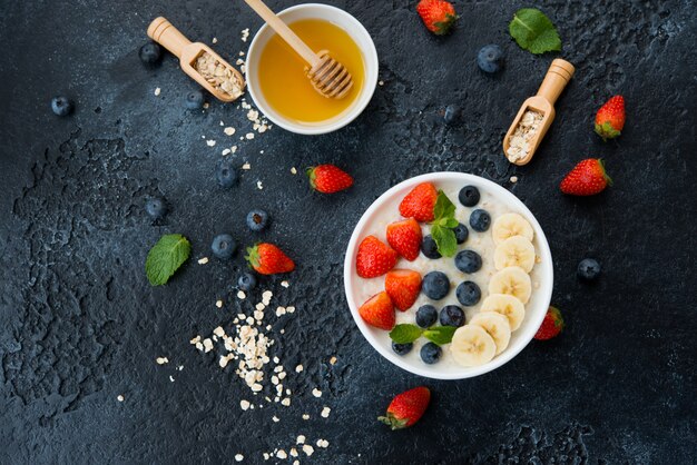 Delicious, healthy and balanced Breakfast of oatmeal with berries and fruit in a plate on the left on a concrete wall. Horizontal orientation with copy space. Top view