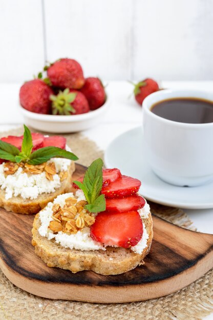 Delicious healthy dietary breakfast: rye bread with cottage cheese and strawberries and a cup of coffee